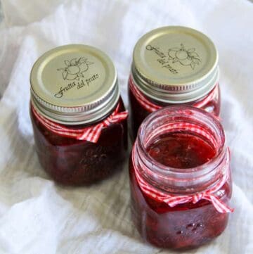 Three jars of strawberry syrup on a white cloth.