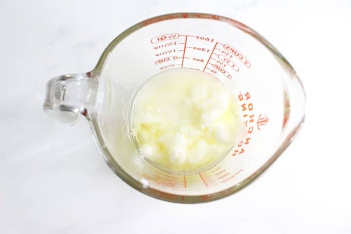 Glass measuring cup containing semi-solid white substance on a white surface.