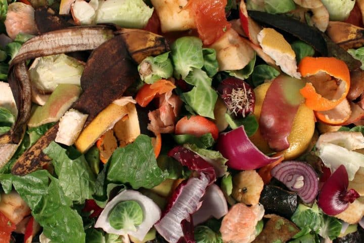 A variety of fruit and vegetable scraps, including banana peels, lettuce leaves, and onion pieces, are piled together.