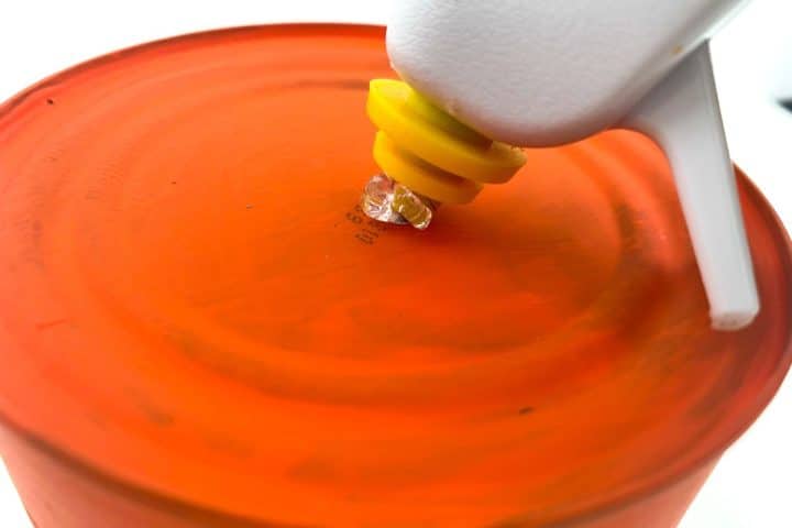 A hot glue gun applying a drop of glue onto an orange surface.