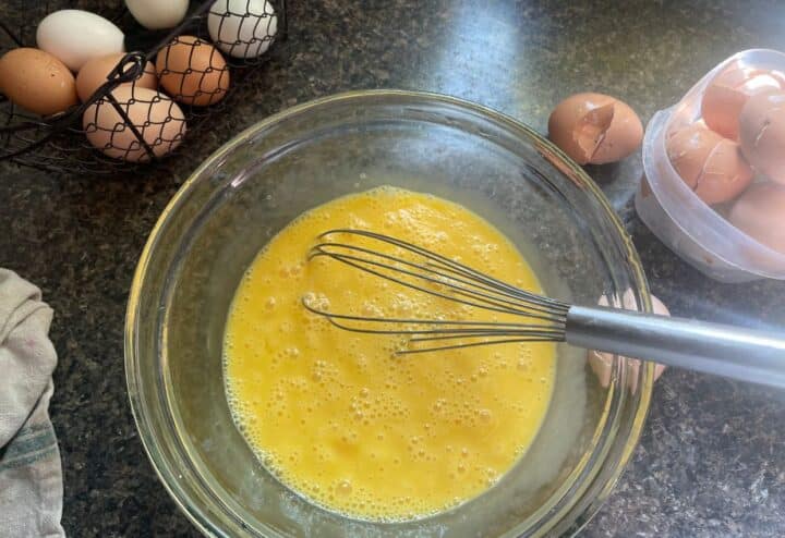 Raw eggs in glass bowl with whisk.