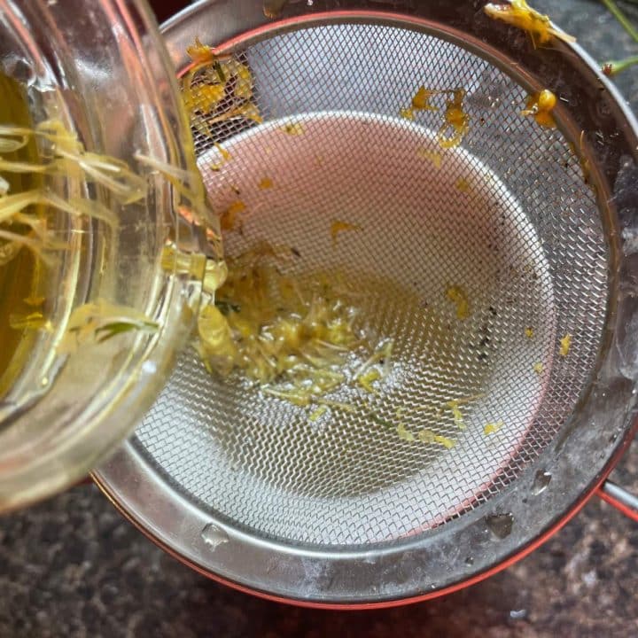 A strainer filled with water and petals of dandelion flowers.