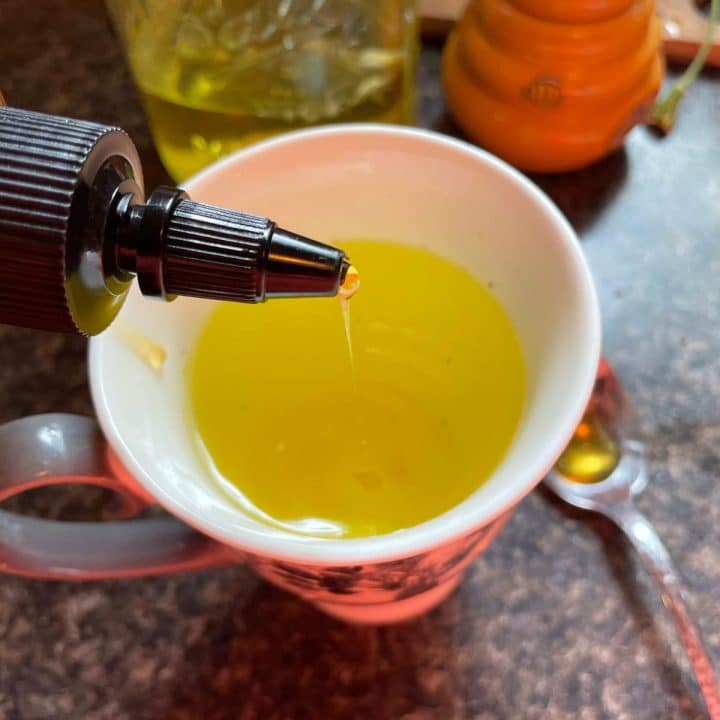 A bottle of olive oil is being poured into a mug.