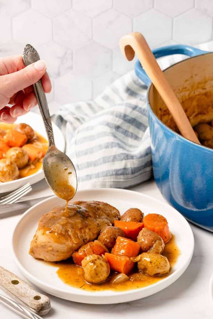 A person prepares a delectable meal by pouring savory gravy onto a plate of Dutch oven chicken breast and carrots.