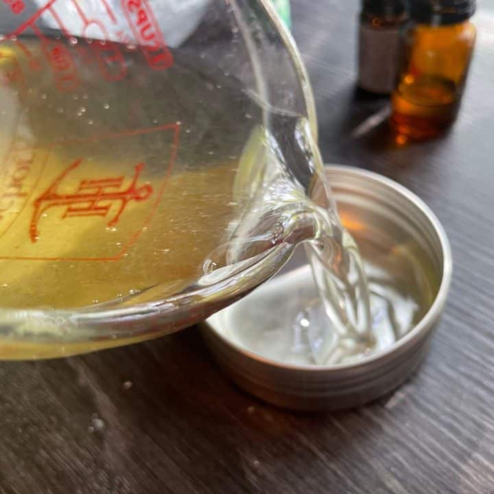 A bottle of essential oil is being poured into a tin.