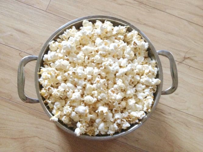 A metal pot filled with popped popcorn, perfect for pioneer Christmas crafts for kids, sits on a light wooden floor.