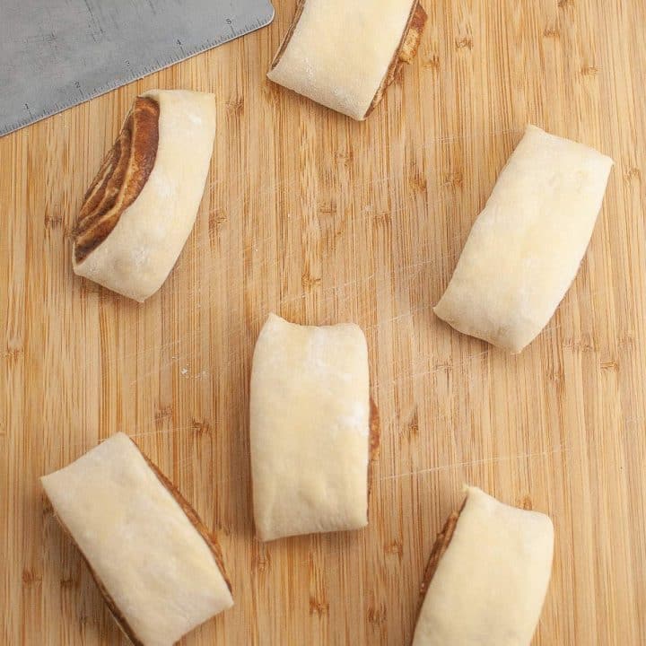 Unbaked cinnamon rolls arranged on a wooden cutting board.