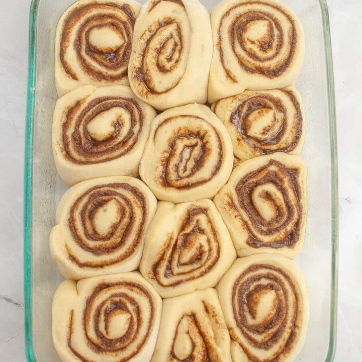 Unbaked cinnamon rolls arranged in a glass baking dish.