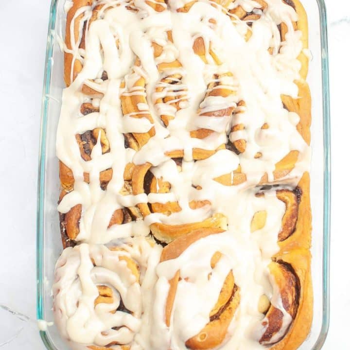 A tray of freshly baked cinnamon rolls with white icing drizzle.