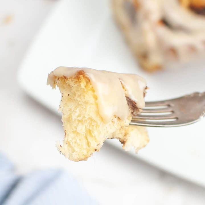 A piece of glazed sourdough cinnamon roll on a fork showcasing its fluffy interior.