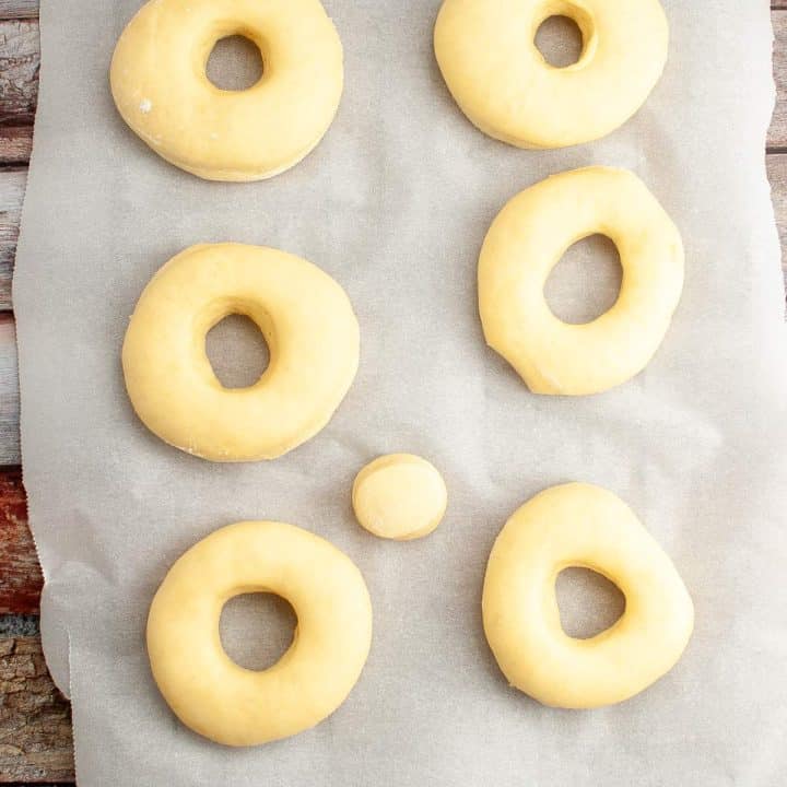 Uncooked sourdough shaped into donuts on parchment paper.
