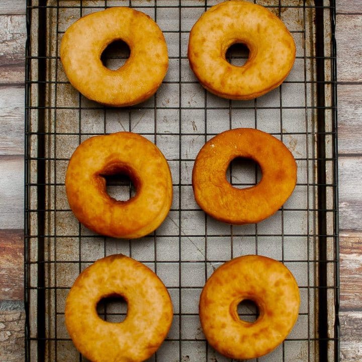 Six freshly baked sourdough donuts cooling on a wire rack.