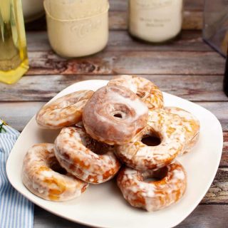 A plate of glazed sourdough doughnuts on a wooden table, with jars of milk in the background.