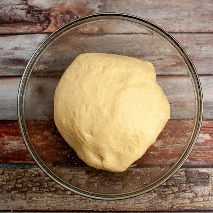 Unbaked sourdough dough resting in a glass bowl on a wooden surface.