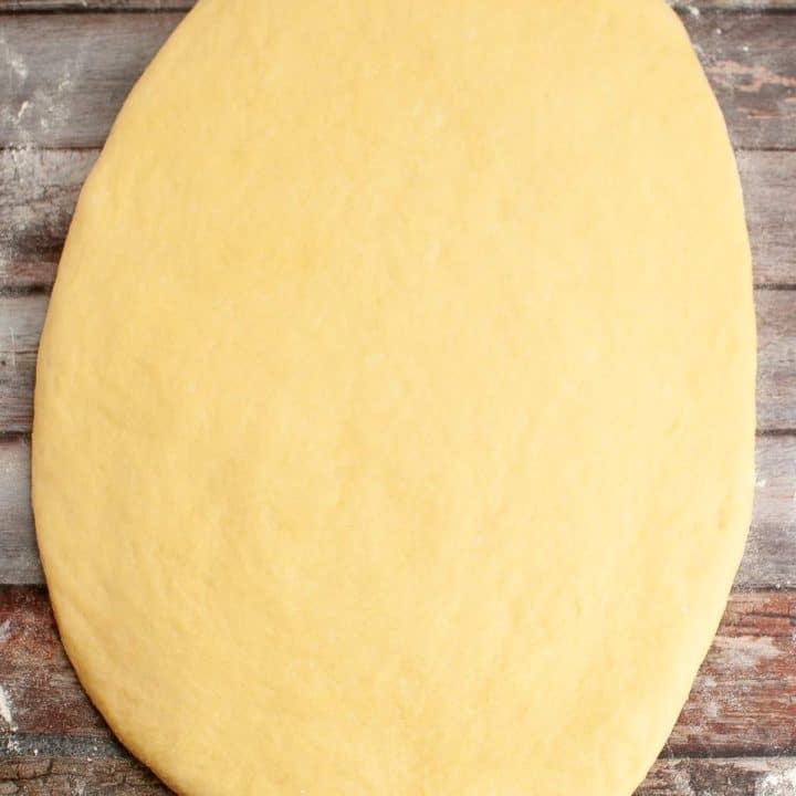 A raw, rolled-out dough on a wooden surface.