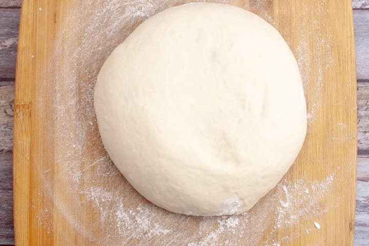 A ball of kneaded dough on a floured wooden board, ready for baking.