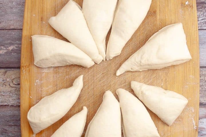 Raw, uncooked triangular dough arranged in a circular pattern on a wooden board.