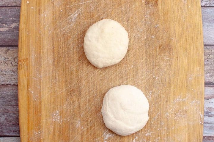 Two balls of raw dough on a floured wooden cutting board.