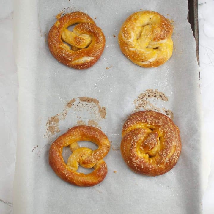 Four freshly baked soft pretzels on parchment paper, some with visible salt crystals.
