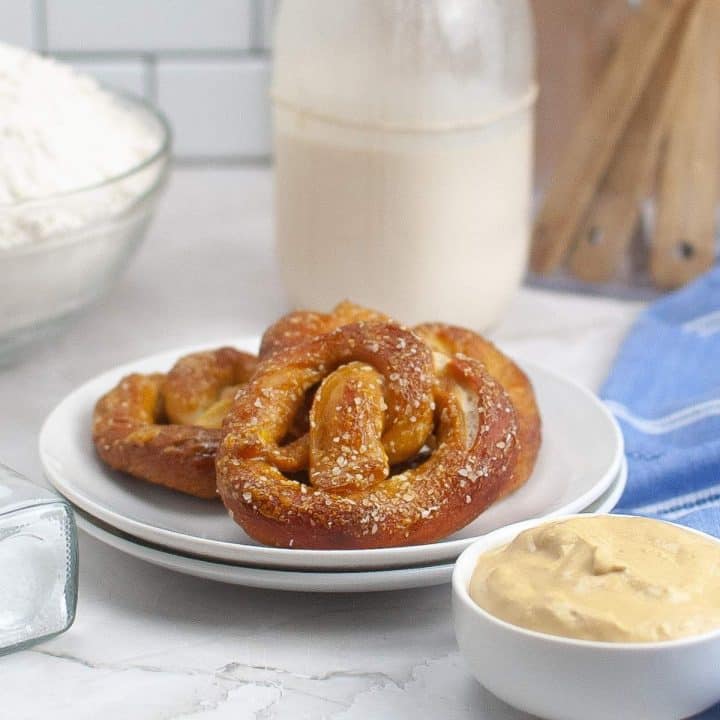 A freshly baked pretzel served with mustard on a kitchen countertop.