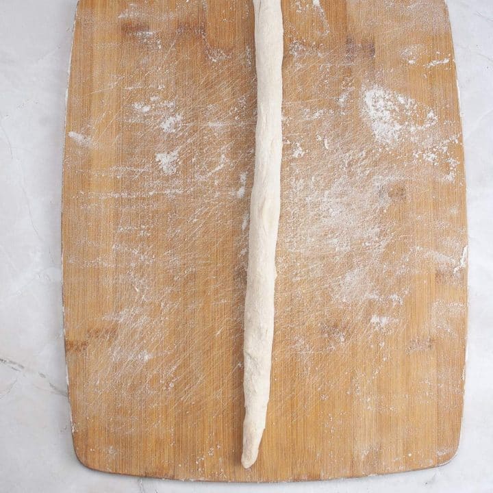 A rolled piece of dough on a floured wooden cutting board.