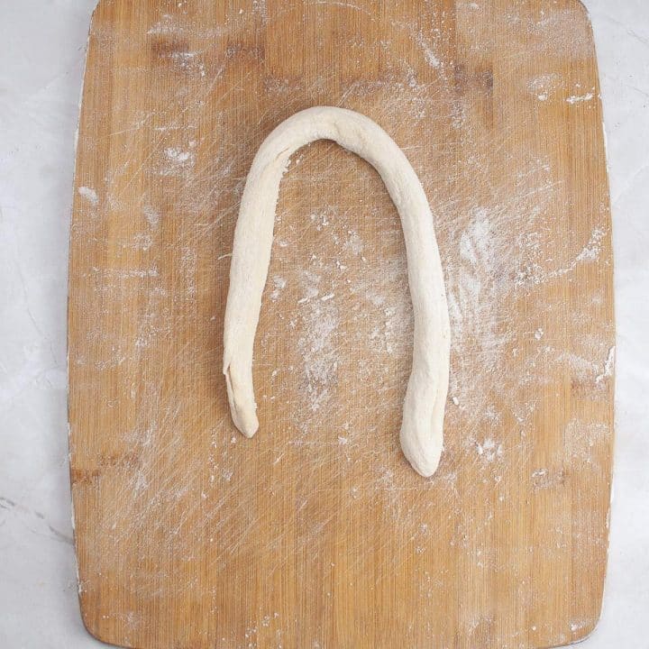 A strip of dough shaped into an 'n' on a floured wooden cutting board.