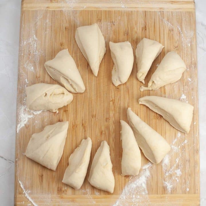 Unbaked croissants arranged on a wooden board dusted with flour.