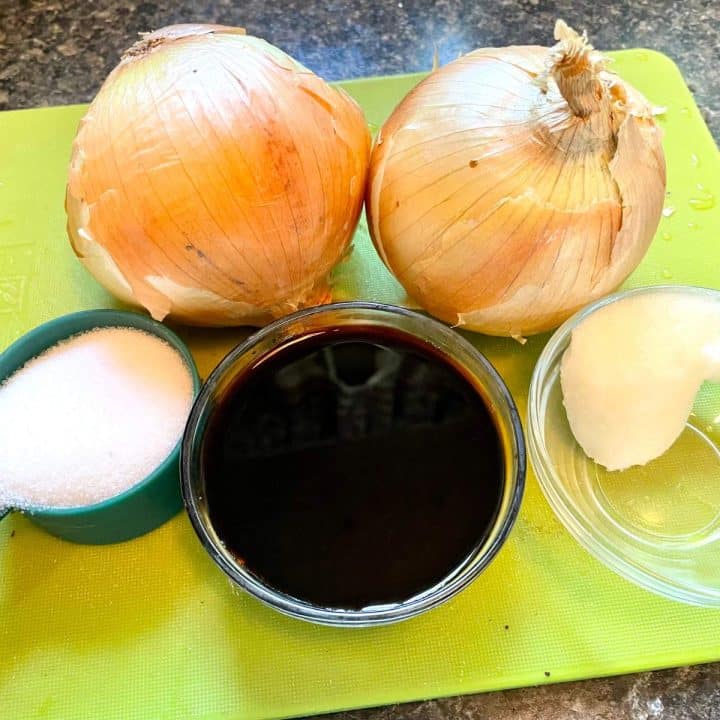 A cutting board with onions, sugar, and soy sauce.