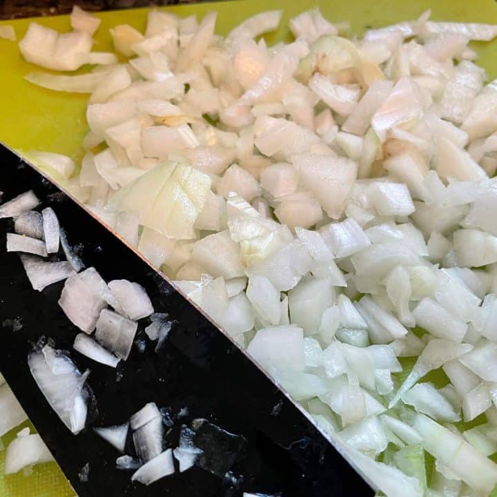 Chopped onions on a cutting board with a knife.