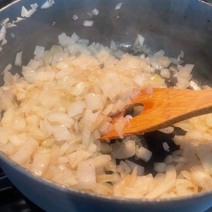 Onions in a pan with a wooden spoon.
