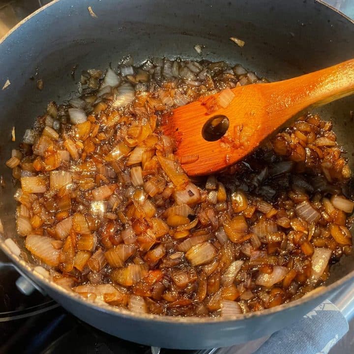 A pan with onions and a wooden spoon in it for making onion relish recipe for canning.