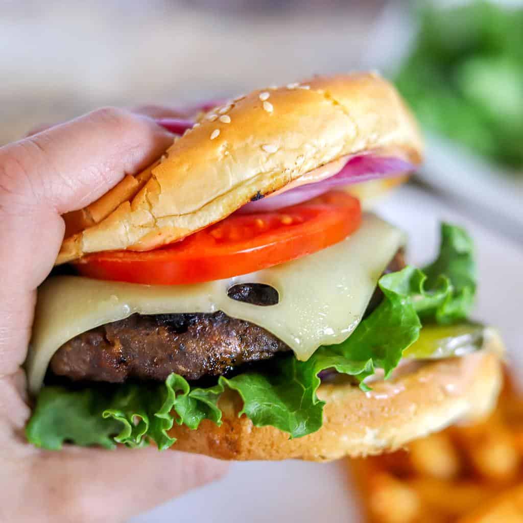A meat and potato pasty cut in half on a white plate, with gravy poured on the plate and a jar of extra gravy in the background—perfect for those seeking hearty venison dinner ideas.
