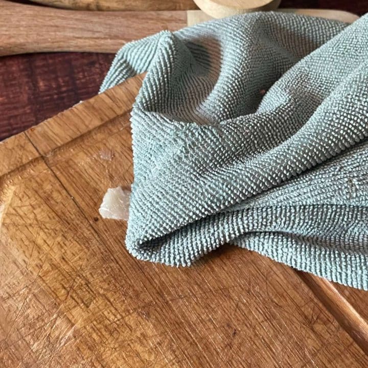 A green cloth on top of a wooden cutting board.